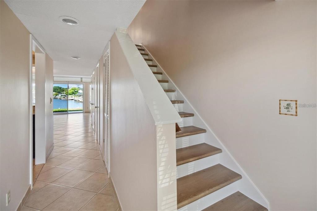 A hallway with tiled floors leads to a waterfront view past a wooden staircase — 44 CLUBHOUSE DRIVE UNIT 105, PALM COAST, FL