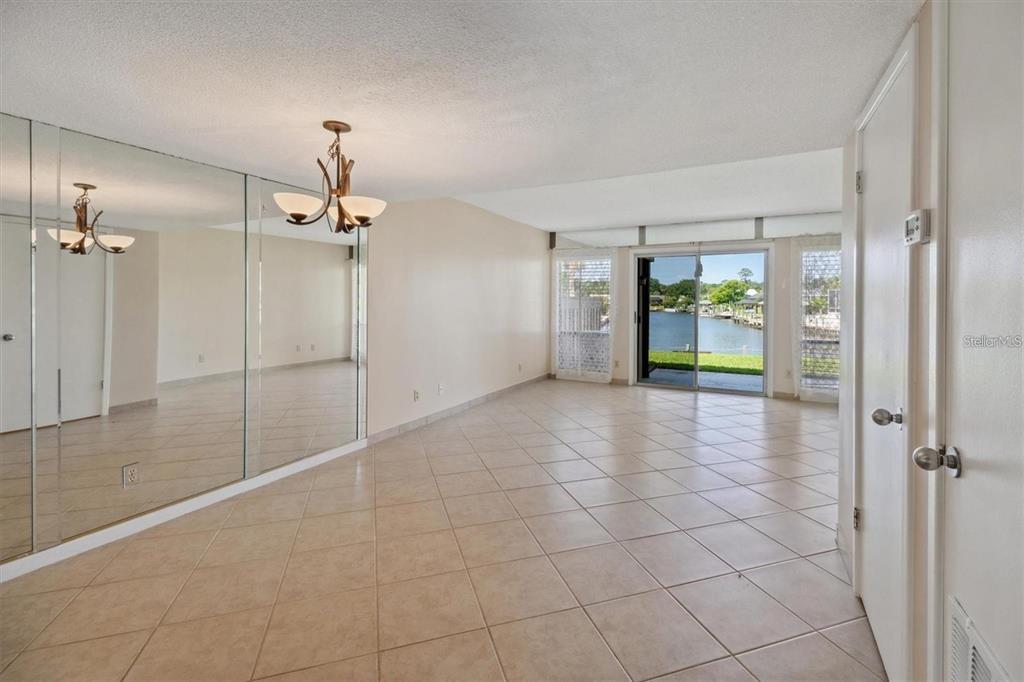 An empty room with tiled floors, a mirrored wall, a chandelier, and sliding glass doors — 44 CLUBHOUSE DRIVE UNIT 105, PALM COAST, FL