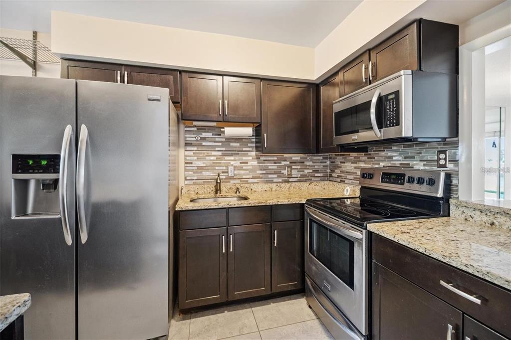 A kitchen featuring dark wood cabinets, stainless steel appliances, and granite countertops — 44 CLUBHOUSE DRIVE UNIT 105, PALM COAST, FL