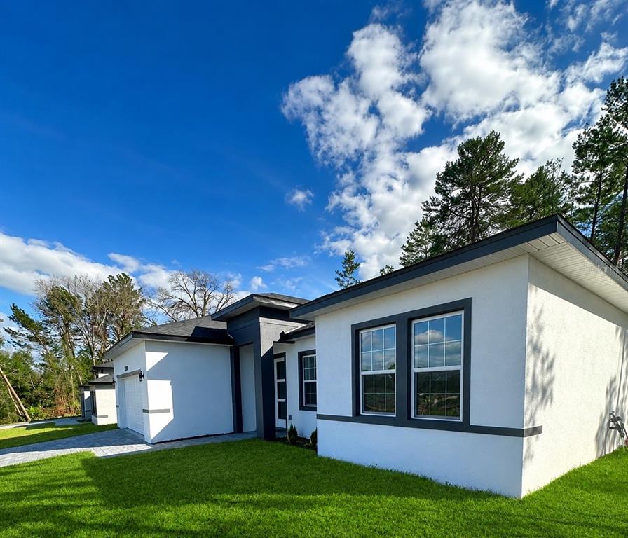 A modern white house with dark trim and a paved driveway under a blue sky — 15001 SW 46TH CIR, OCALA, FL