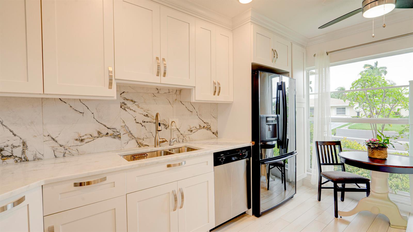 A kitchen with white cabinets, marble-patterned backsplash, stainless steel appliances, and a small dining table — 8638 Bella Vista Drive, Boca Raton FL 33433, BOCA RATON, FL
