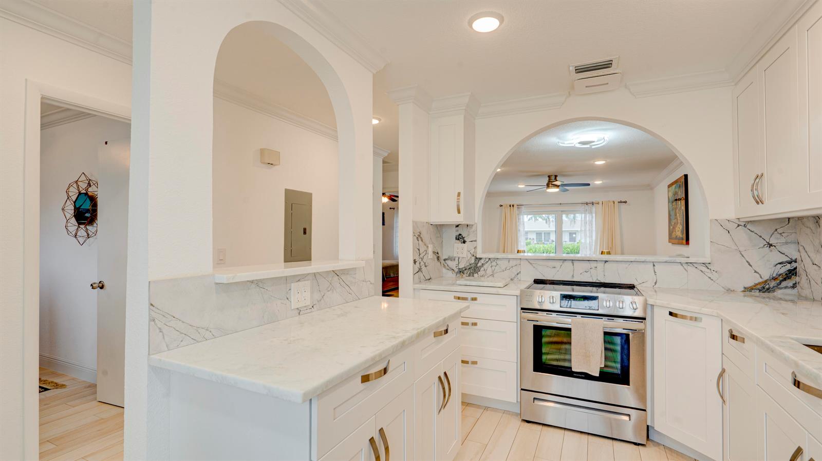 A white kitchen features marble countertops, stainless steel appliances, and an arched pass-through window — 8638 Bella Vista Drive, Boca Raton FL 33433, BOCA RATON, FL