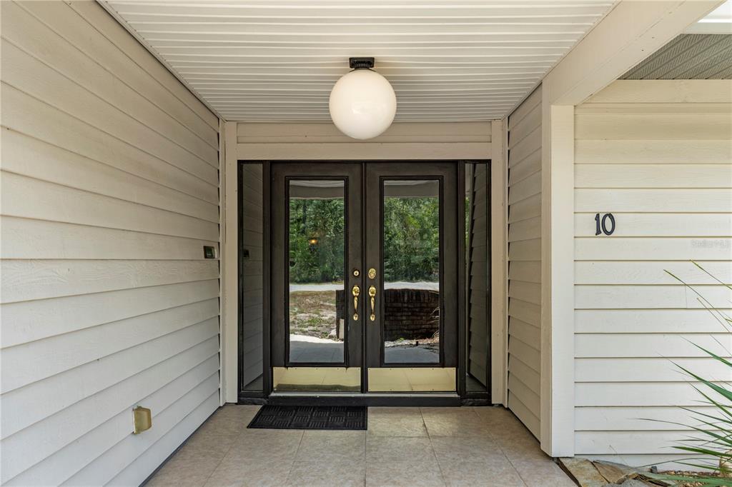 A covered entryway features double glass doors, a globe light, and light-colored horizontal siding — 10 SYCAMORE COURT S, HOMOSASSA, FL