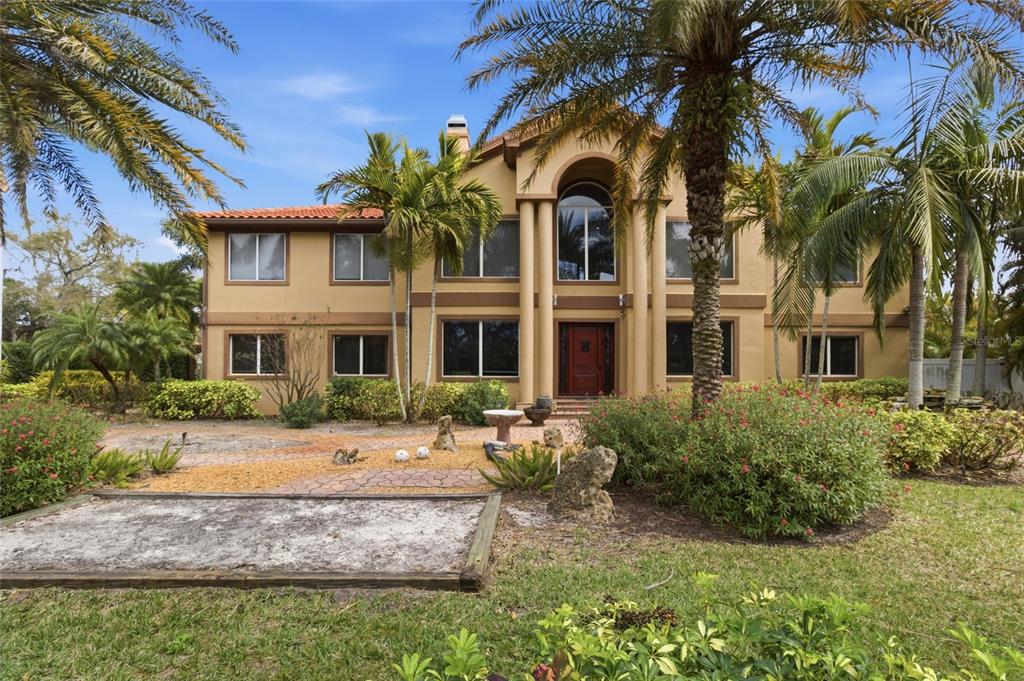 A two-story tan house with a tiled roof, arched entryway, and palm trees in front — 303 SUNNY LANE, BELLEAIR, FL