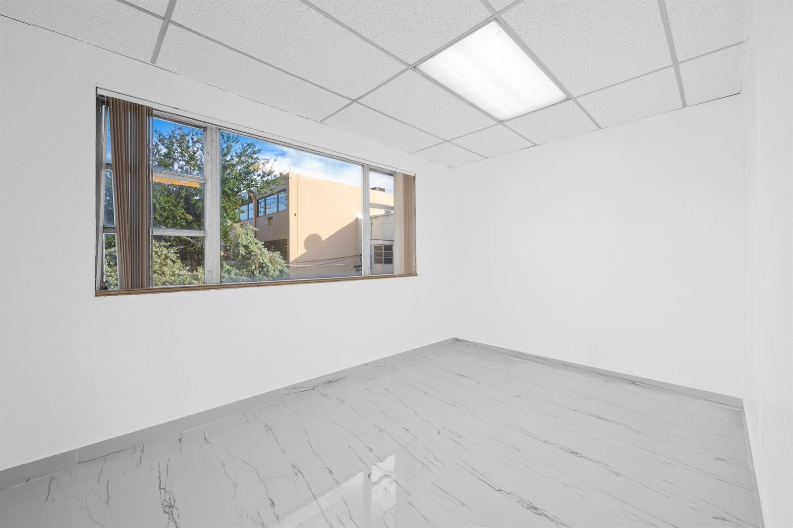 An empty office room with white walls, marble-patterned tile flooring, and a large window — 2601 E Atlantic Boulevard, Pompano Beach FL 33062, POMPANO BEACH, FL