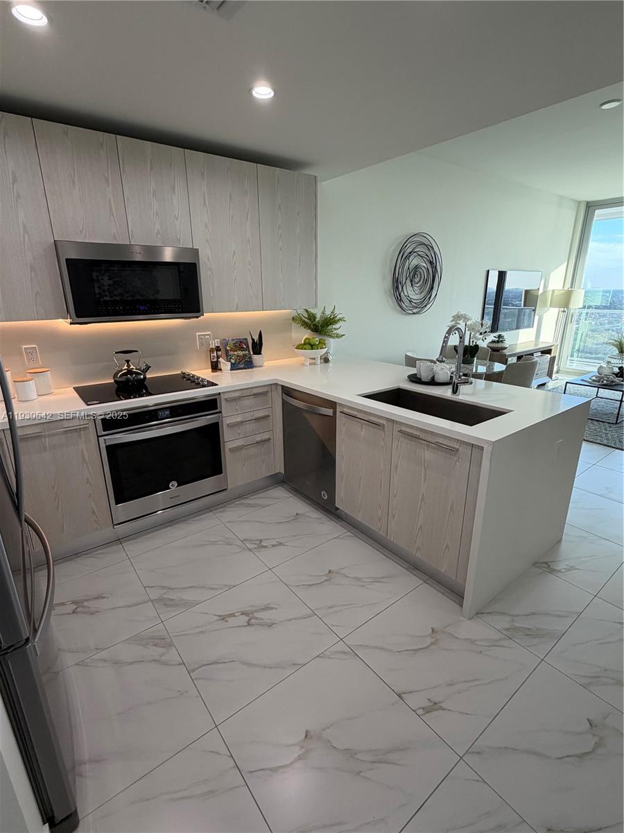 A modern kitchen features light wood cabinets, white countertops, stainless steel appliances, and marble-patterned tile flooring — 2000 Metropica Way # 2108, Sunrise FL 33323, SUNRISE, FL