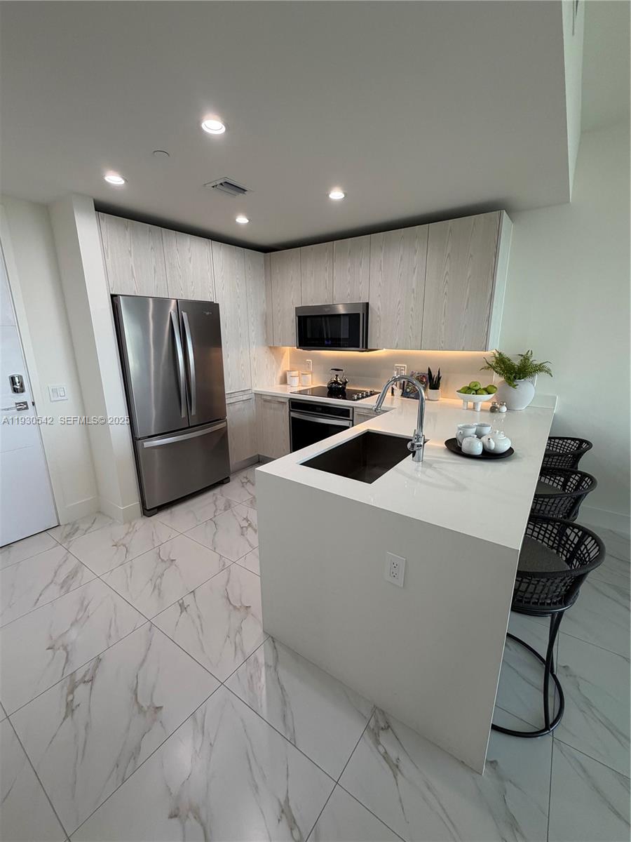 A modern kitchen features light wood cabinets, stainless steel appliances, and a white quartz island — 2000 Metropica Way # 2108, Sunrise FL 33323, SUNRISE, FL