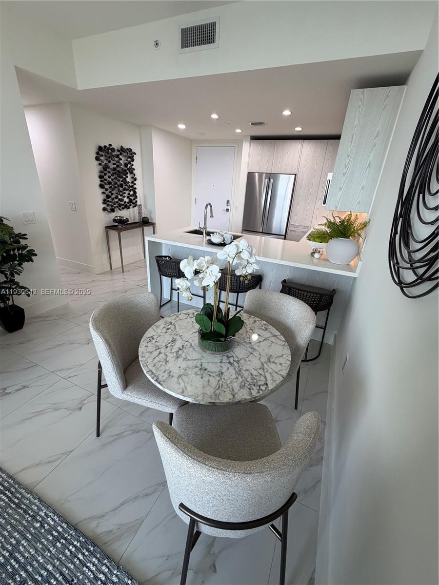 A dining area with a marble table and chairs sits before an open kitchen island — 2000 Metropica Way # 2108, Sunrise FL 33323, SUNRISE, FL