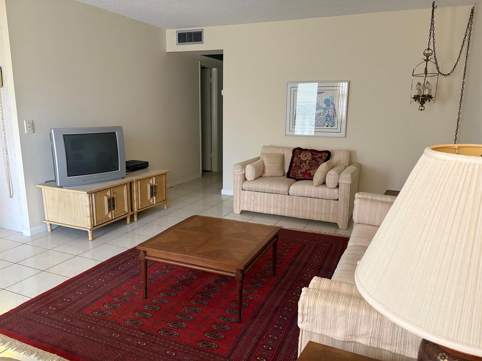 A living room features a red patterned rug, two beige sofas, and a television console — 2036 Cornwall B # 2036, Boca Raton FL 33434, BOCA RATON, FL