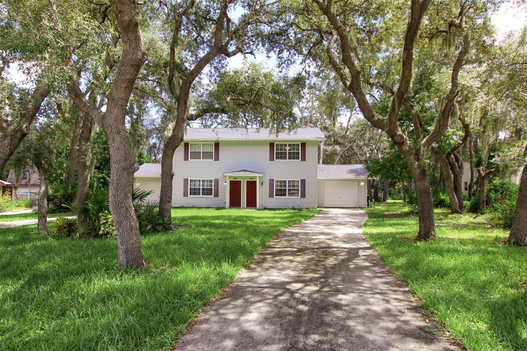 A two-story house with light siding, a concrete driveway, and large trees in the yard — 3818 RED OAK COURT, LAKE WALES, FL