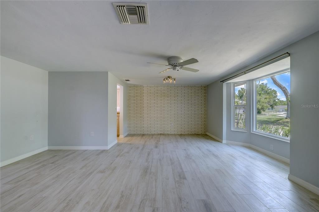A living room with light wood-look flooring, a white brick accent wall, and large windows — 3024 CHASE CIRCLE, SARASOTA, FL