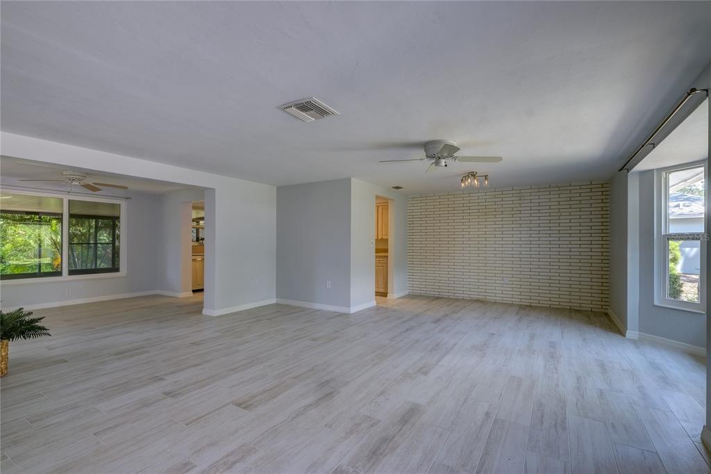 A spacious living room features light wood-look tile flooring, a white brick wall, and ceiling fans — 3024 CHASE CIRCLE, SARASOTA, FL