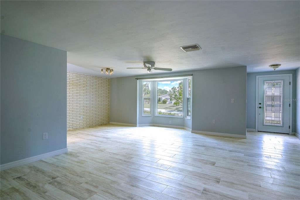 A living room with light blue walls, wood-look tile flooring, a brick accent wall, and windows — 3024 CHASE CIRCLE, SARASOTA, FL