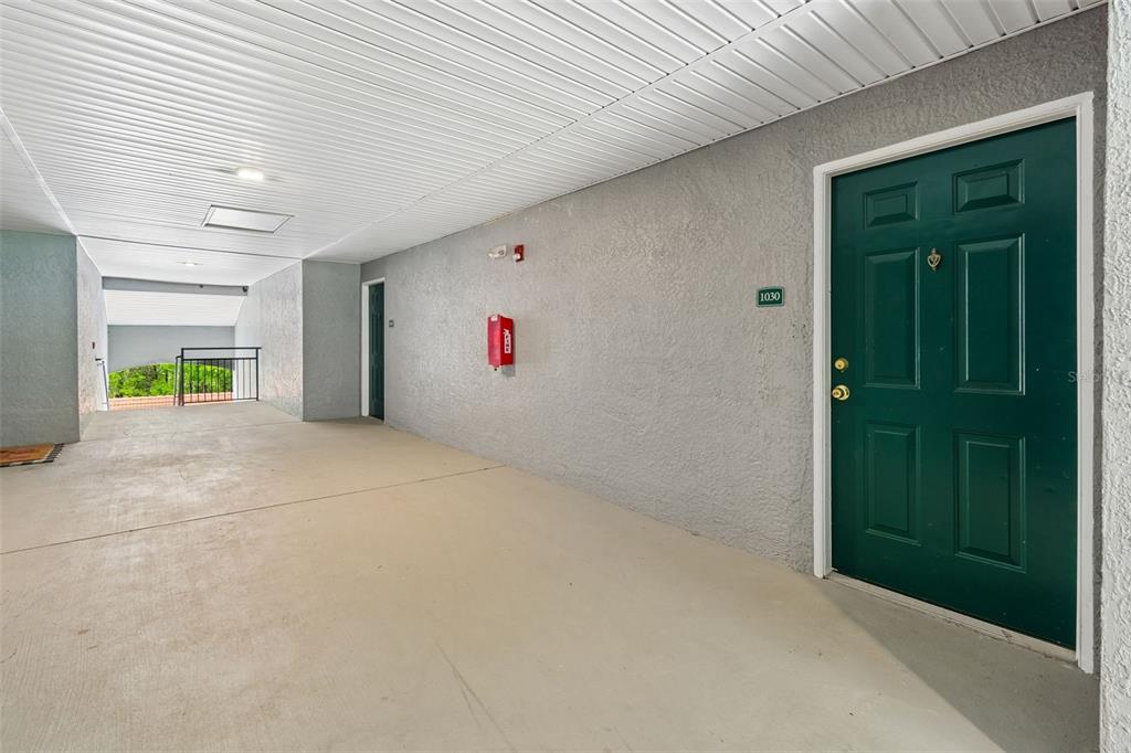 A covered outdoor walkway leads to a green apartment door labeled 1030 — 18001 RICHMOND PLACE DRIVE UNIT 1030, TAMPA, FL