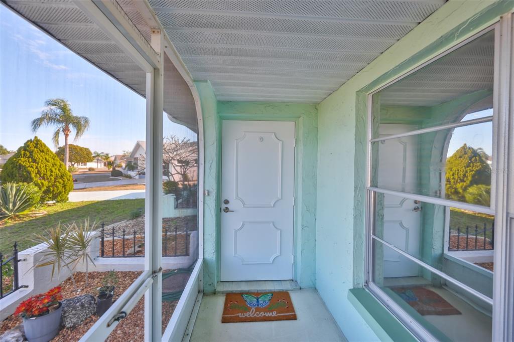 A screened-in front porch features a white door, a welcome mat, and light green walls — 325 GREEN MANOR DRIVE, SUN CITY CENTER, FL