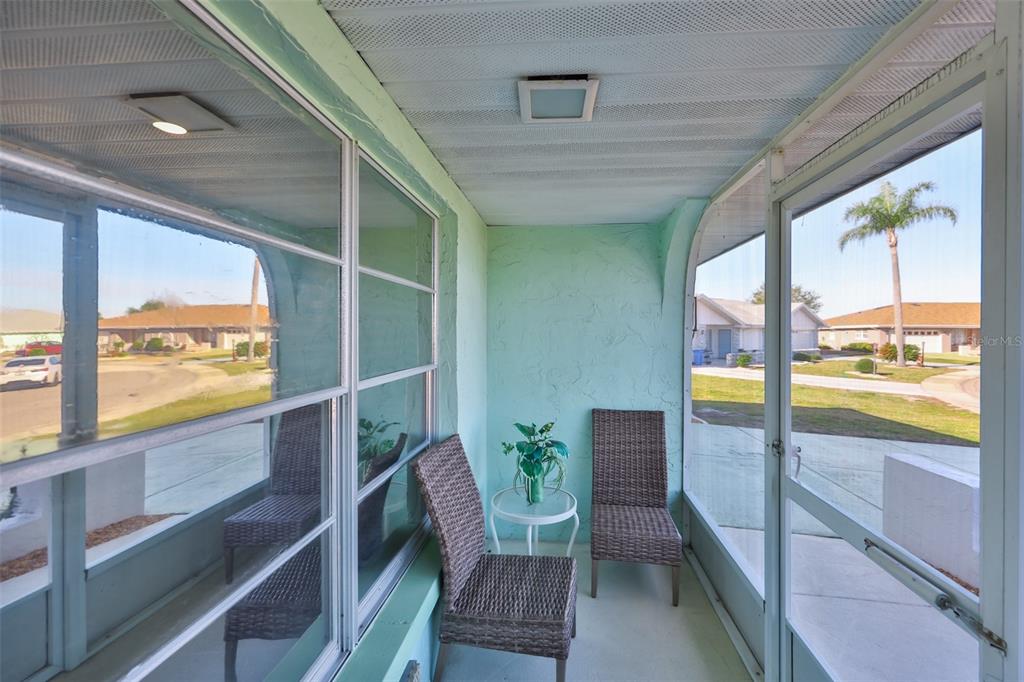A screened-in porch with light green walls, two wicker chairs, and a small side table — 325 GREEN MANOR DRIVE, SUN CITY CENTER, FL