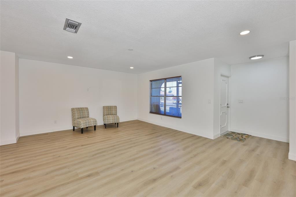 A bright, empty living room features light wood-look flooring, white walls, and two patterned chairs — 325 GREEN MANOR DRIVE, SUN CITY CENTER, FL