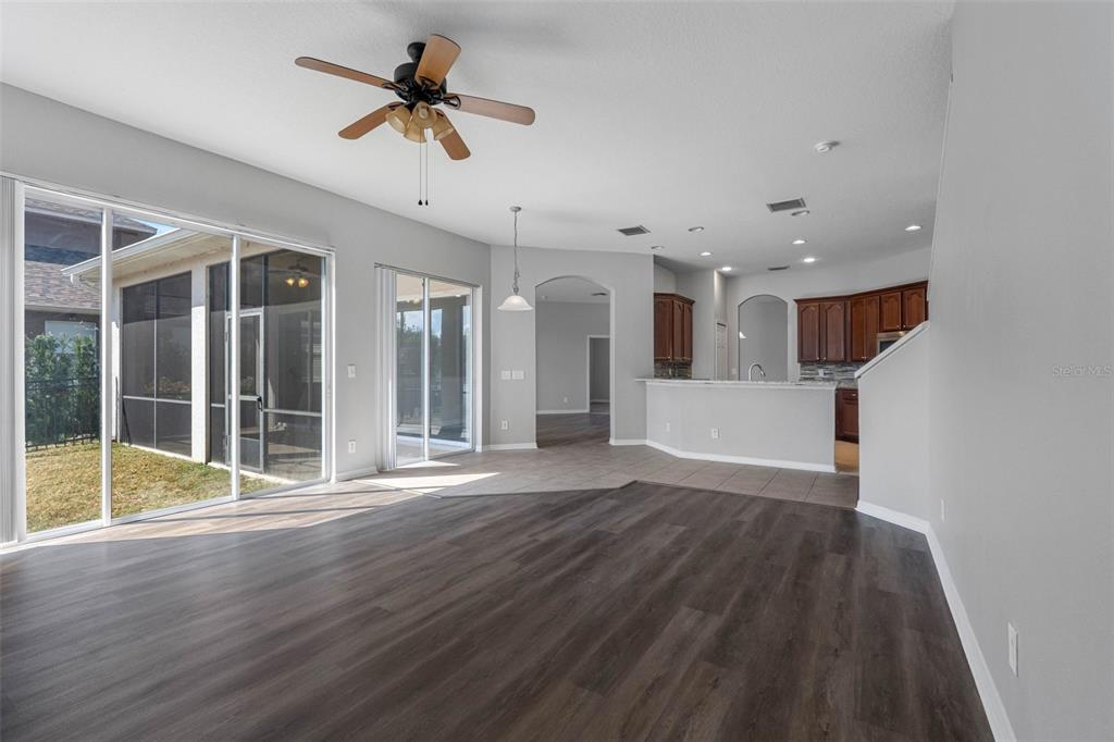 An open-concept living area features dark wood-look flooring, a ceiling fan, and a kitchen — 4820 PORTMARNOCK WAY, WESLEY CHAPEL, FL