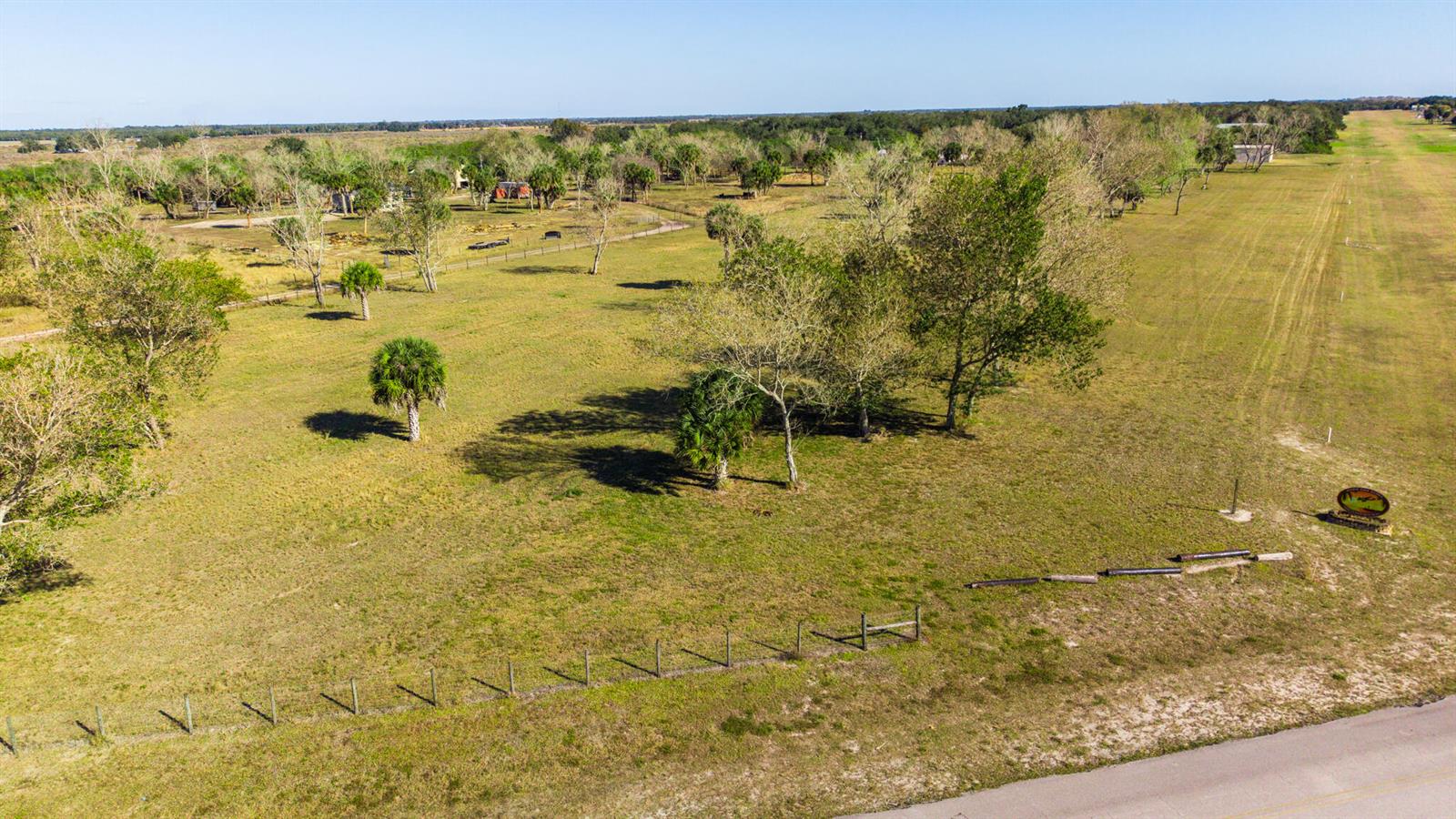 An aerial view shows a grassy, fenced lot with scattered trees and a nearby road — 0 SW 144th Parkway, Okeechobee FL 34974, OKEECHOBEE, FL