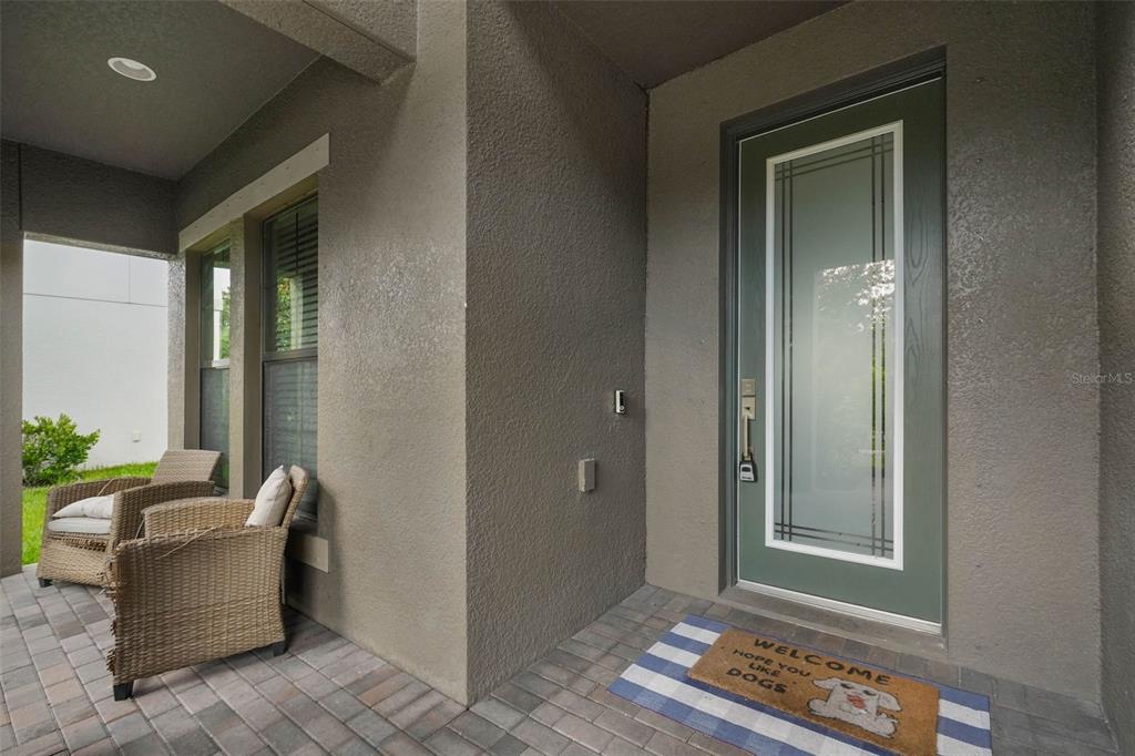 A covered porch features a green front door, wicker chairs, and a dog-themed welcome mat — 13134 MONACH ISLES DRIVE, RIVERVIEW, FL