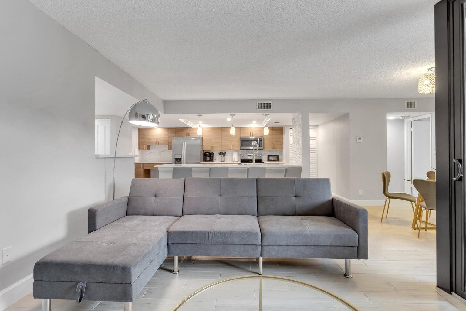 A gray sectional sofa faces an open-concept kitchen with light wood cabinets and a breakfast bar — 955 Dotterel Road, Delray Beach FL 33444, DELRAY BEACH, FL