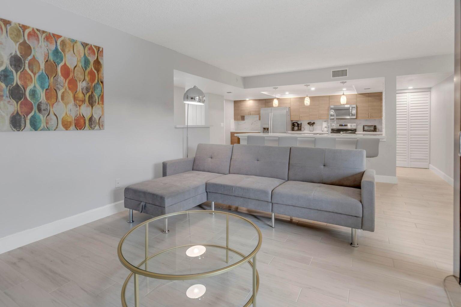 A living room with a gray sectional sofa and glass coffee table faces an open kitchen — 955 Dotterel Road, Delray Beach FL 33444, DELRAY BEACH, FL