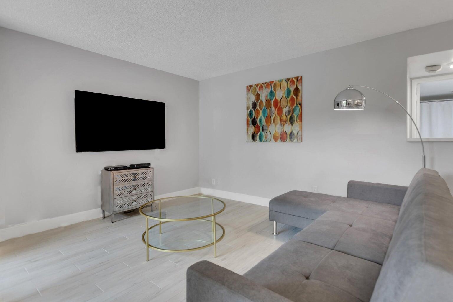 A living room features light wood-look tile floors, a grey sectional sofa, and a wall-mounted television — 955 Dotterel Road, Delray Beach FL 33444, DELRAY BEACH, FL