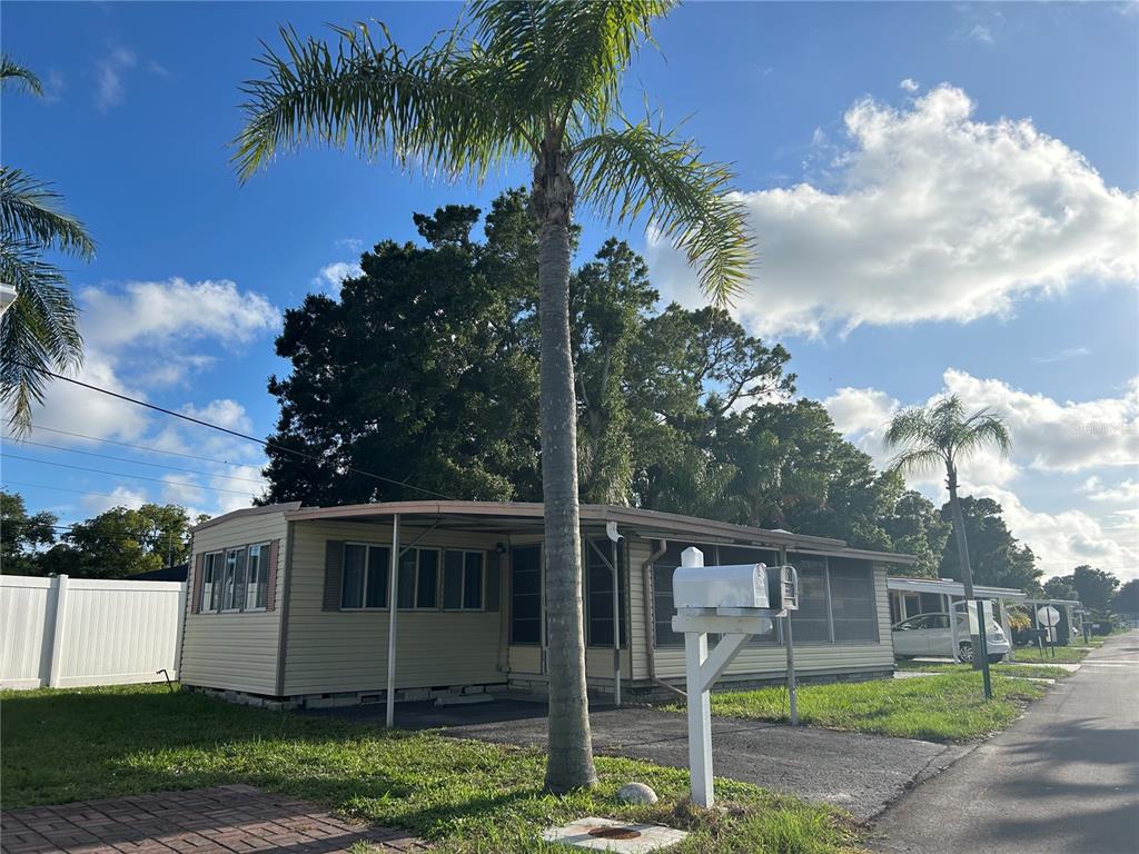 A single-story mobile home with light siding, a screened porch, and a palm tree out front — 12674 SEMINOLE BOULEVARD UNIT S18, LARGO, FL