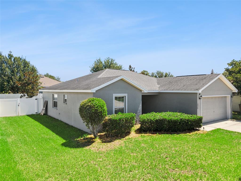 A gray, single-story house with a shingled roof, a garage, and a manicured front lawn — 1920 COUNTRY MANOR STREET, BARTOW, FL