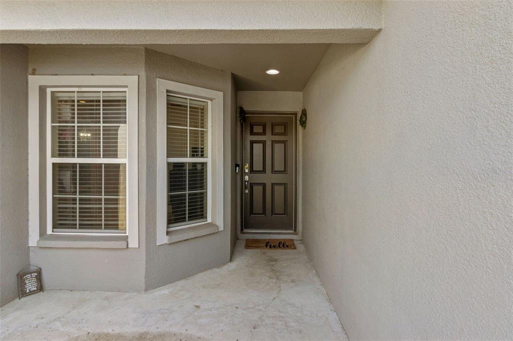 A covered entryway features a dark brown front door, a bay window, and concrete flooring — 1920 COUNTRY MANOR STREET, BARTOW, FL