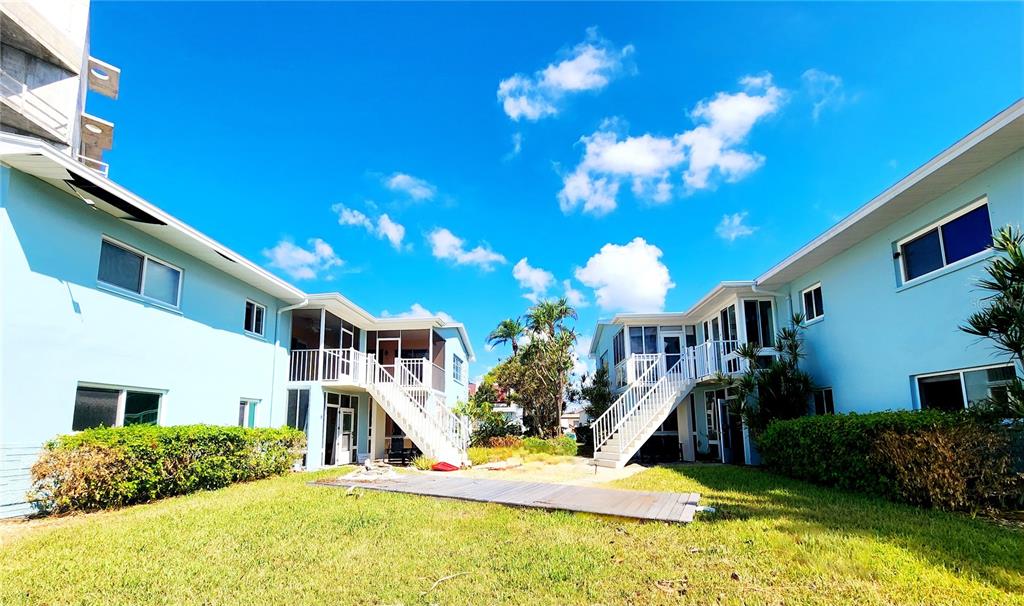 Exterior view of two light blue apartment buildings with white staircases and a grassy courtyard — 241 SKIFF POINT UNIT 4, CLEARWATER BEACH, FL