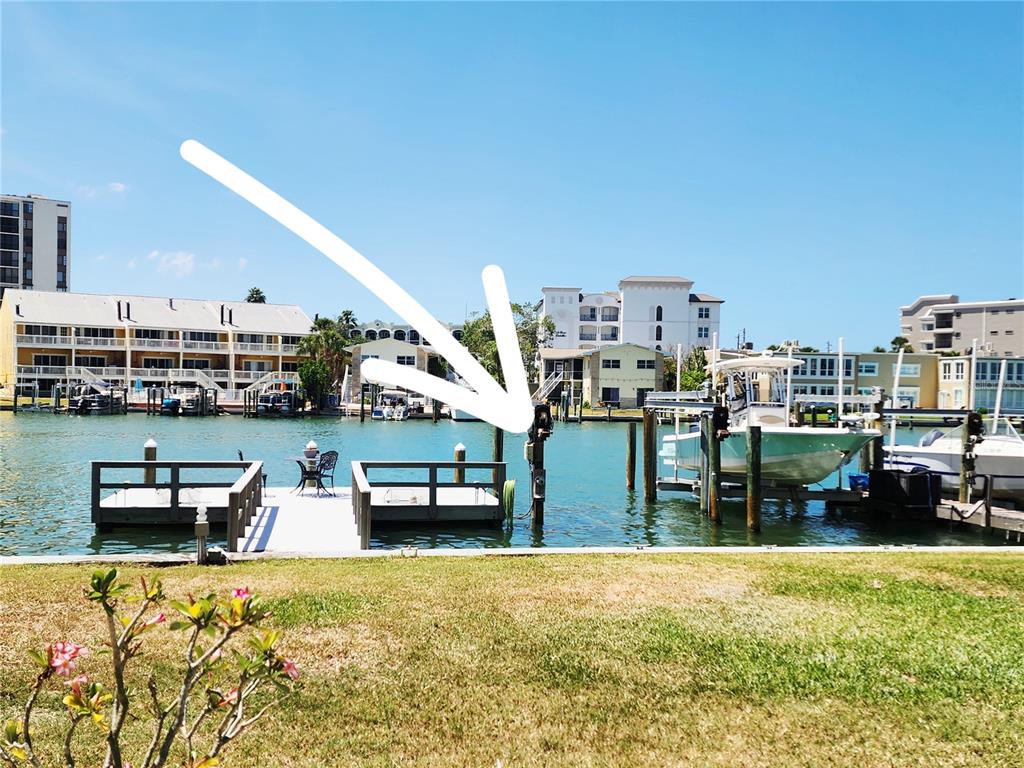 A view of a waterfront dock with a boat lift and residential buildings in the background — 241 SKIFF POINT UNIT 4, CLEARWATER BEACH, FL