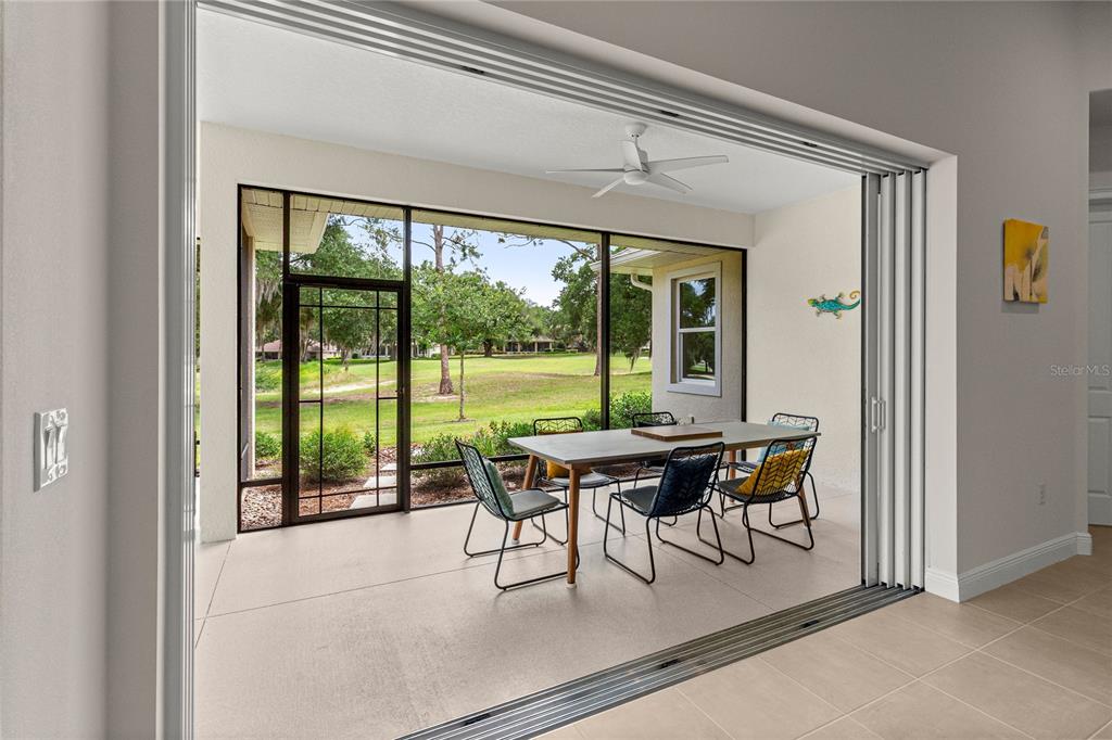 A covered patio with a dining set overlooks a grassy yard through a large screen — 5090 GREENS DRIVE, LADY LAKE, FL