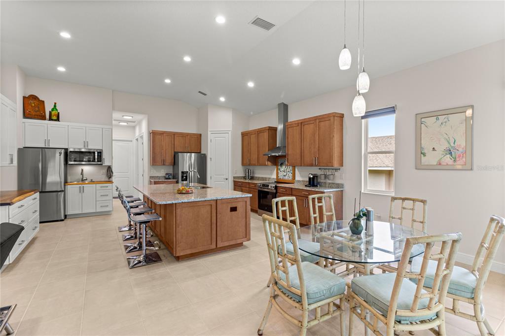 A kitchen features a central island, wood cabinetry, stainless steel appliances, and a dining area — 5090 GREENS DRIVE, LADY LAKE, FL