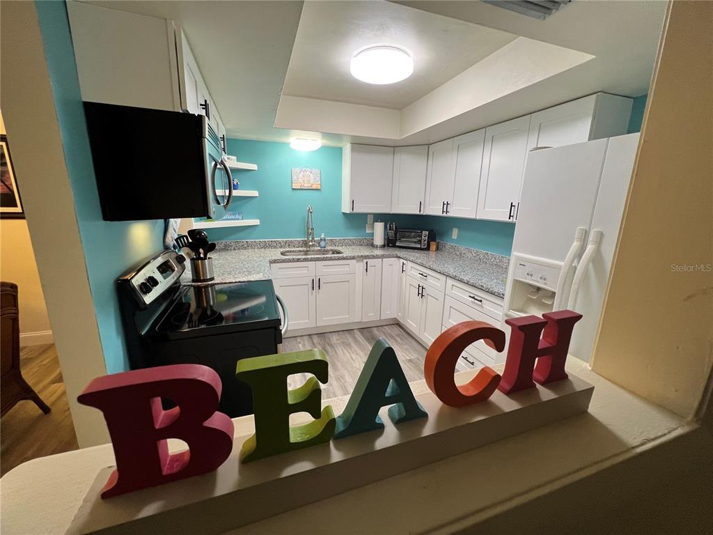 A kitchen features white cabinets, a teal wall, granite countertops, and large decorative letters — 1406 N SATURN AVENUE, CLEARWATER, FL