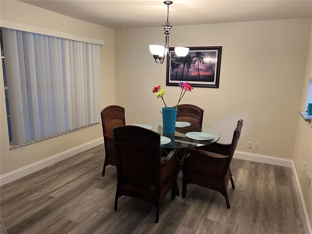 A dining room features a glass-topped table, four wicker chairs, and wood-look flooring — 1406 N SATURN AVENUE, CLEARWATER, FL
