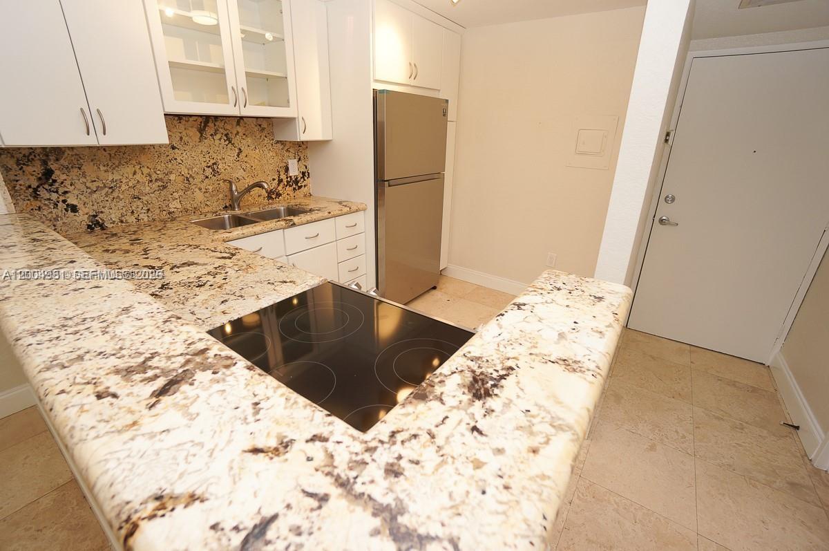 A kitchen features white cabinetry, granite countertops, a stainless steel refrigerator, and a glass cooktop — 1228 West Ave # 513, Miami Beach FL 33139, MIAMI BEACH, FL