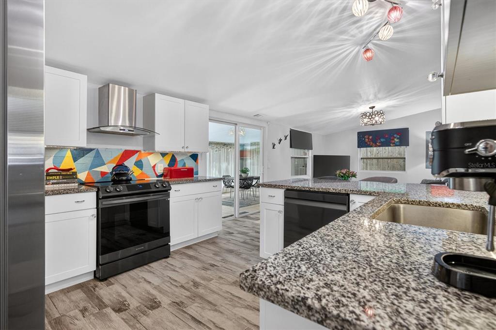 A kitchen with white cabinets, granite countertops, a colorful geometric backsplash, and wood-look flooring — 212 S GLENWOOD AVENUE, ORLANDO, FL