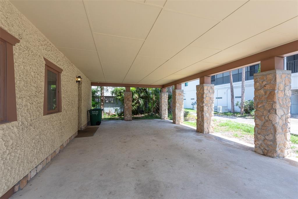 A covered carport with a concrete floor and stone-clad support pillars next to a stucco wall — 205 MAGNOLIA STREET, NEW SMYRNA BEACH, FL