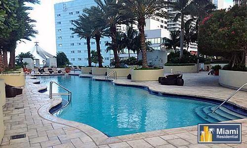 A curved swimming pool surrounded by a stone deck, palm trees, and a large building — 244 Biscayne Blvd # 3004, Miami FL 33132, MIAMI, FL