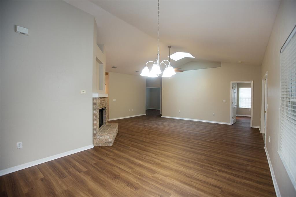 A living room features vaulted ceilings, a brick fireplace, and wood-look flooring — 4314 NW 35TH STREET, GAINESVILLE, FL