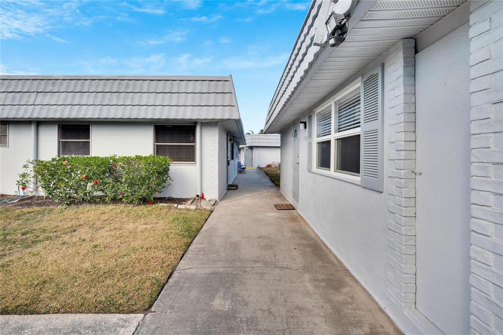A concrete walkway runs between two single-story residential buildings with gray siding and tiled roofs — 202 BEDFORD TRAIL UNIT 112, SUN CITY CENTER, FL
