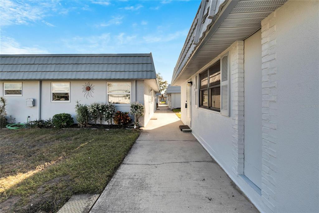 A concrete walkway runs between two single-story residential buildings with gray roofs and light siding — 202 BEDFORD TRAIL UNIT 112, SUN CITY CENTER, FL