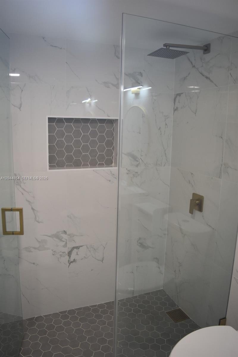 A modern walk-in shower features white marble-look wall tiles, gray hexagonal floor tiles, and gold fixtures — 666 W 81st St # 311, Hialeah FL 33014, HIALEAH, FL