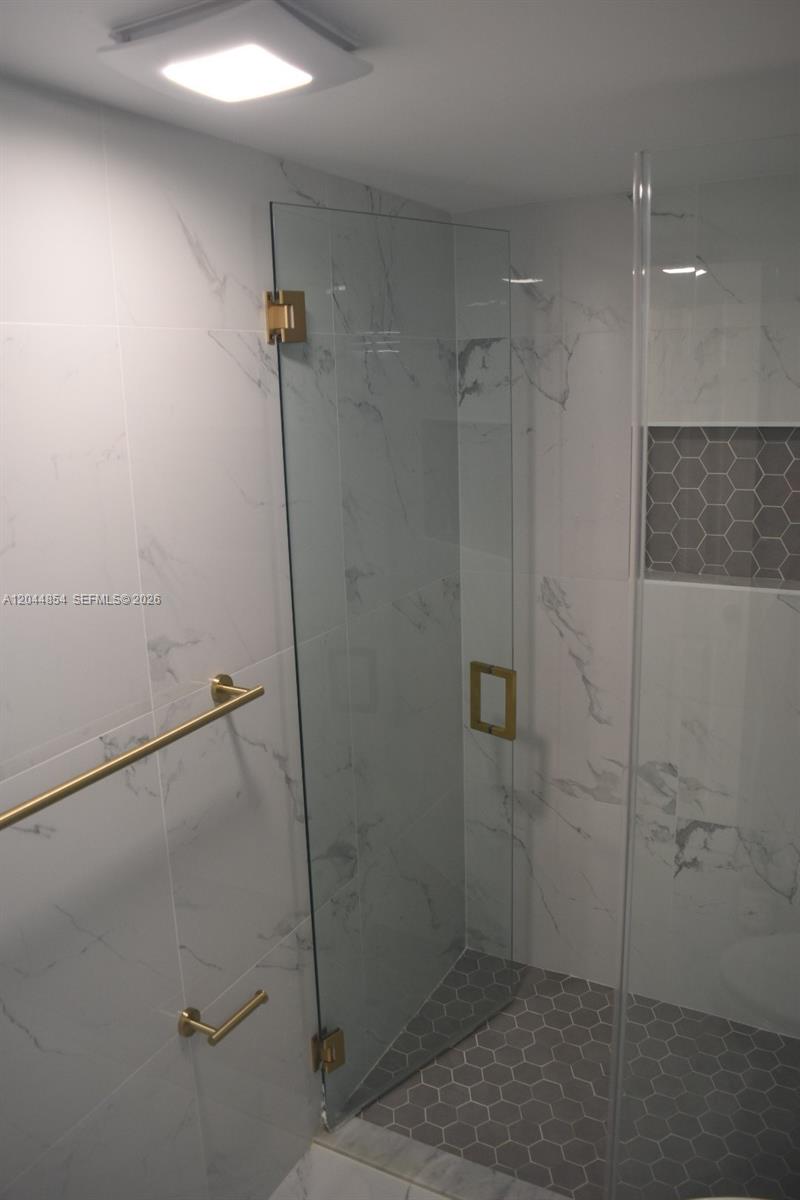 A modern bathroom features a glass shower enclosure, marble-look wall tiles, and gold hardware — 666 W 81st St # 311, Hialeah FL 33014, HIALEAH, FL