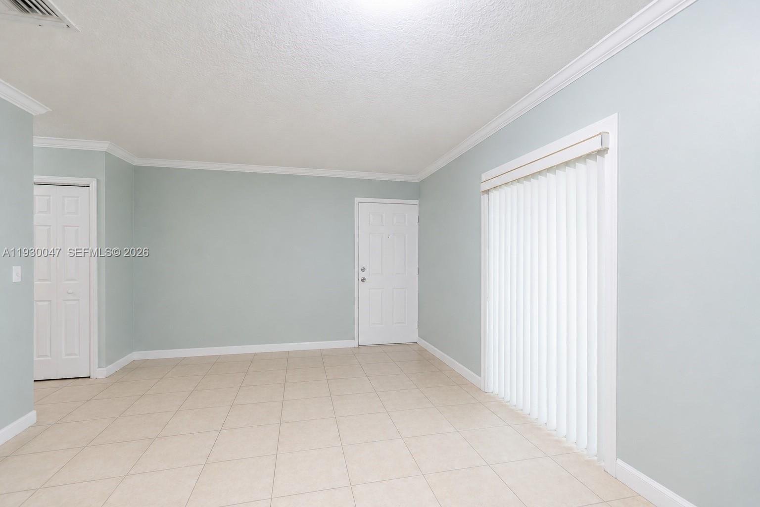 An empty room features light blue walls, tile flooring, a white door, and vertical blinds — 63 NW 17th Pl # 6, Miami FL 33125, MIAMI, FL