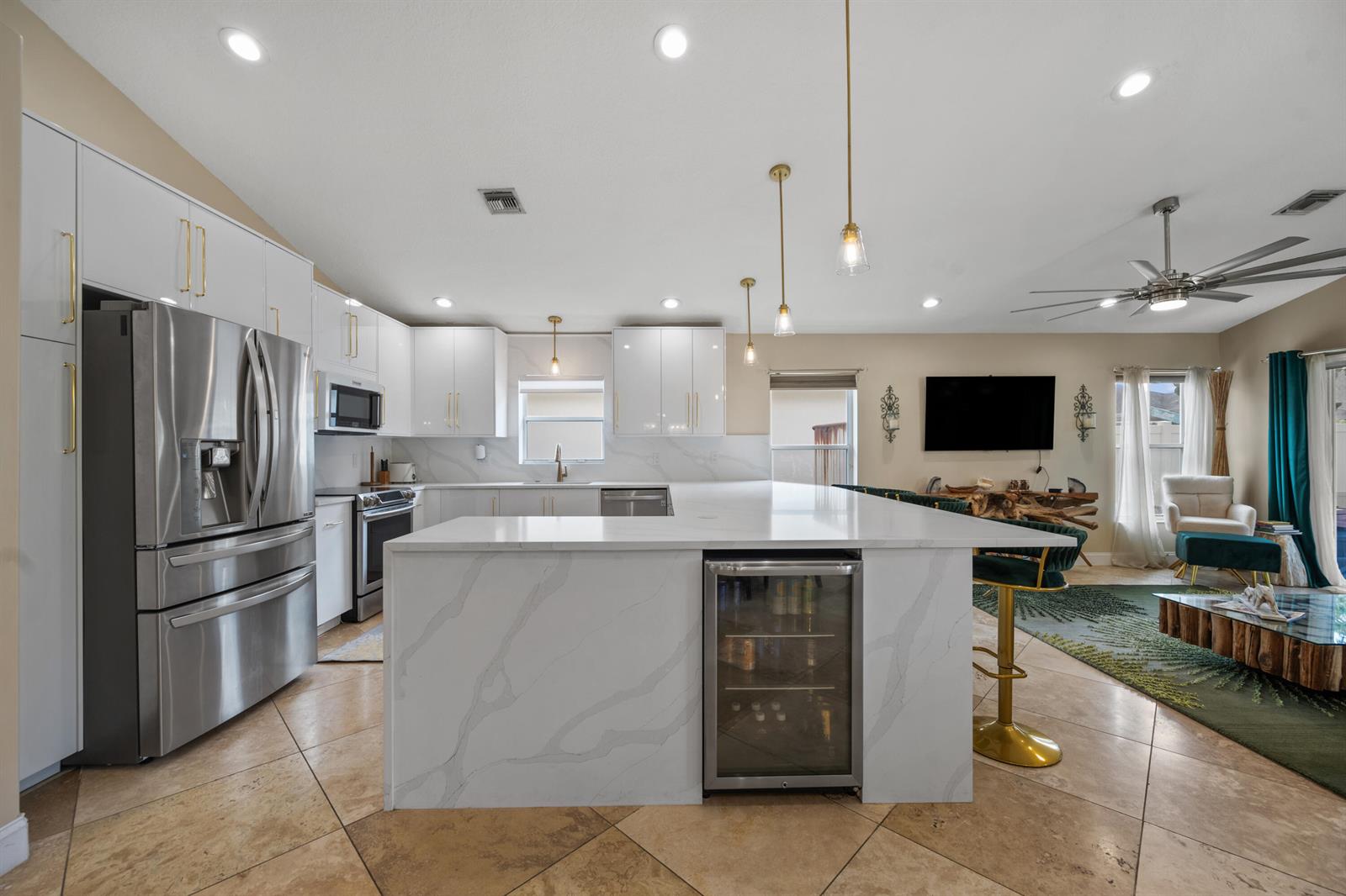 A modern kitchen features white cabinetry, a marble-topped island with a wine cooler, and tile flooring — 1097 Aviary Road, Wellington FL 33414, WELLINGTON, FL