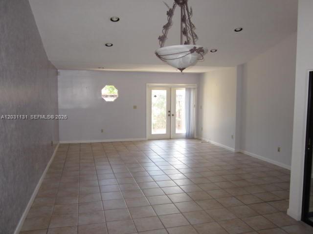 An empty room features light-colored tile flooring, a decorative chandelier, and glass patio doors — 11449 SW 84 LN # 0, Miami FL 33173, MIAMI, FL