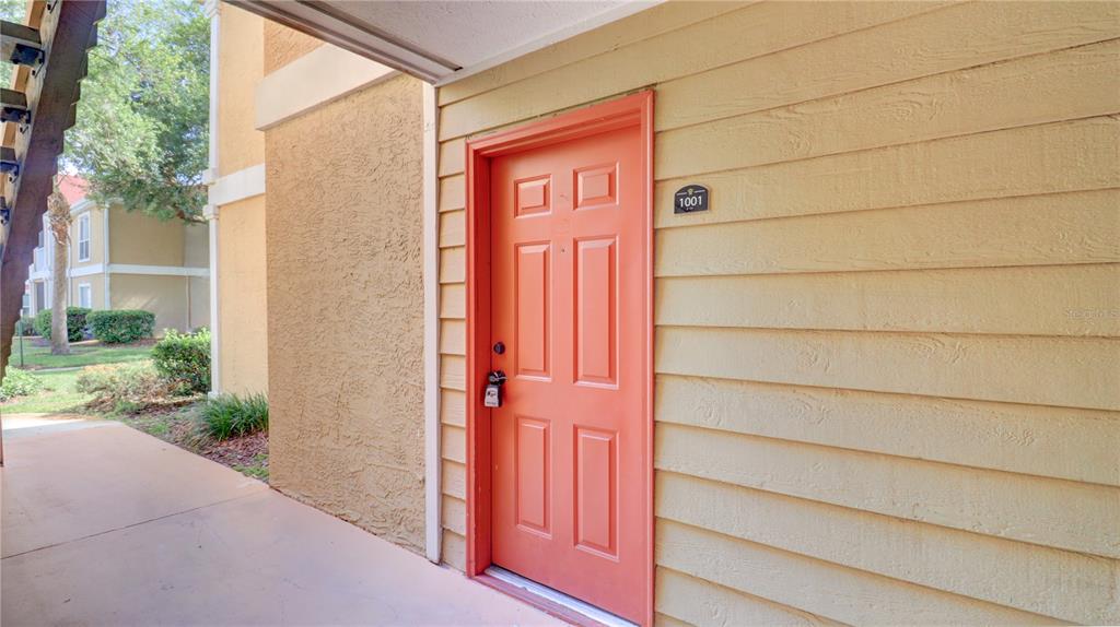 An exterior view of an apartment entrance with a coral-colored door labeled 1001 — 9481 HIGHLAND OAK DRIVE UNIT 1001, TAMPA, FL