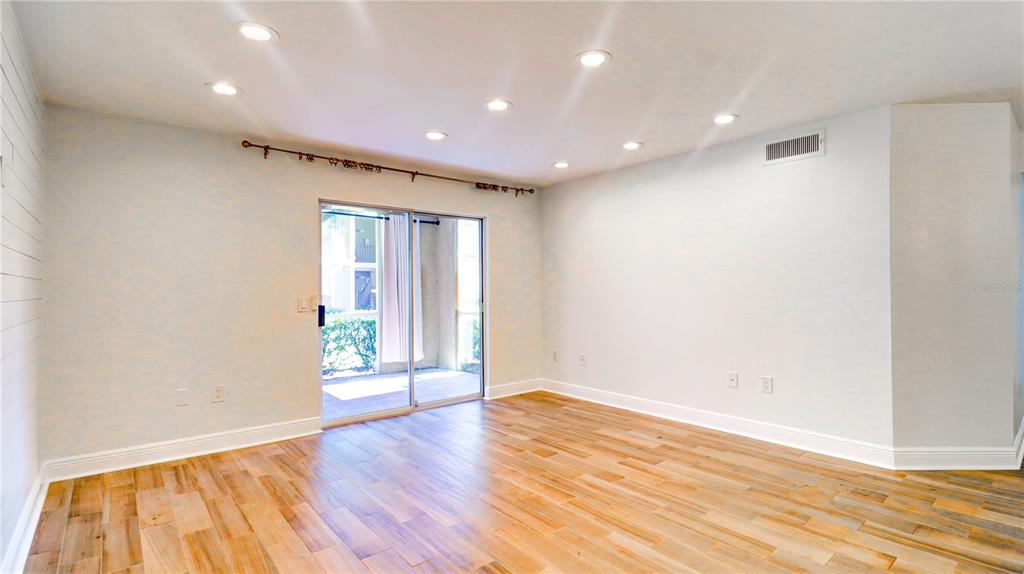 An empty room with light wood-look flooring, recessed lighting, and a sliding glass door — 9481 HIGHLAND OAK DRIVE UNIT 1001, TAMPA, FL